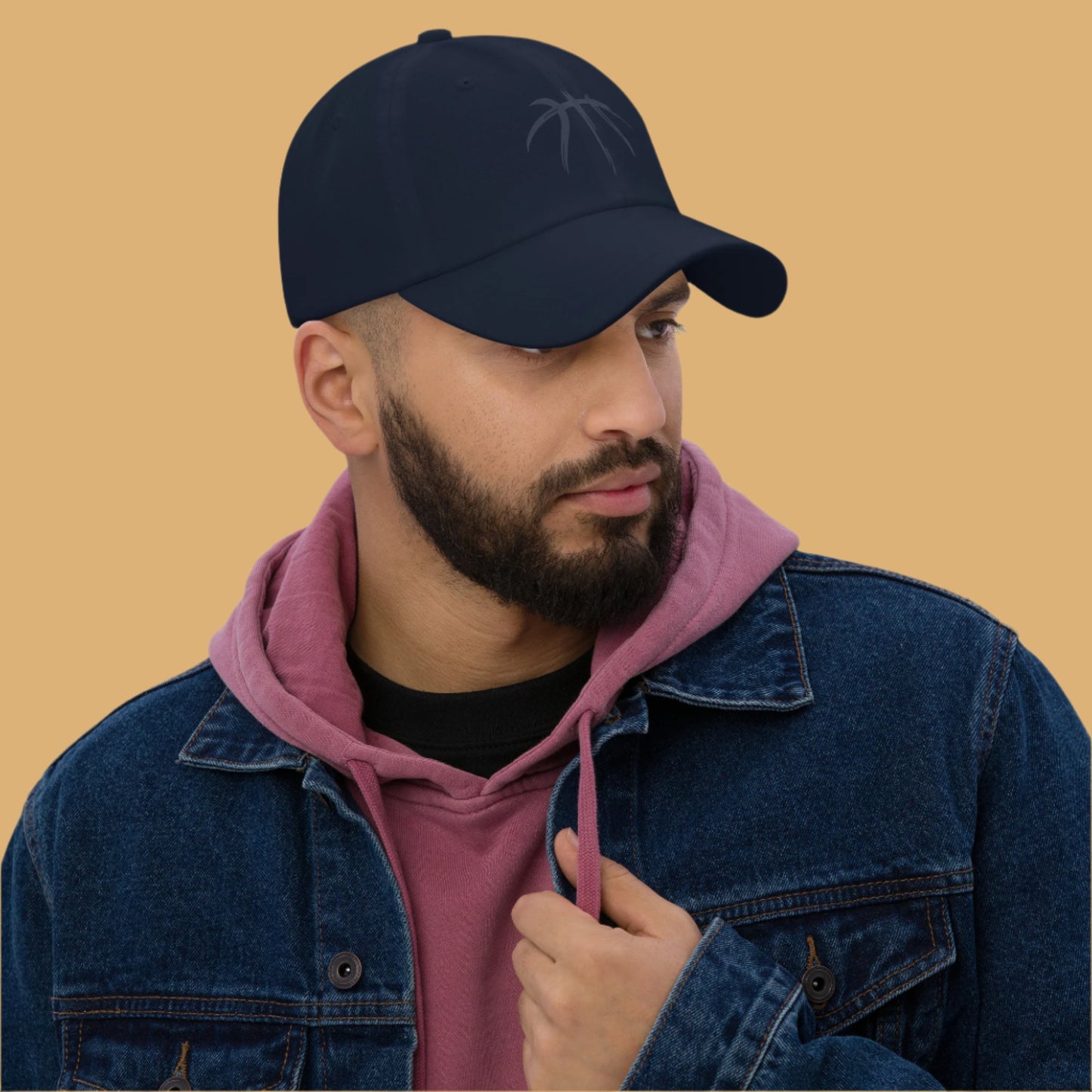 Man wearing a navy cap, pink hoodie, and denim jacket on a gray background