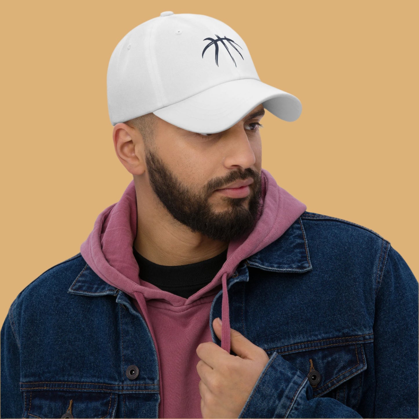 Man wearing a white cap with a logo, denim jacket, and pink hoodie against a gray background
