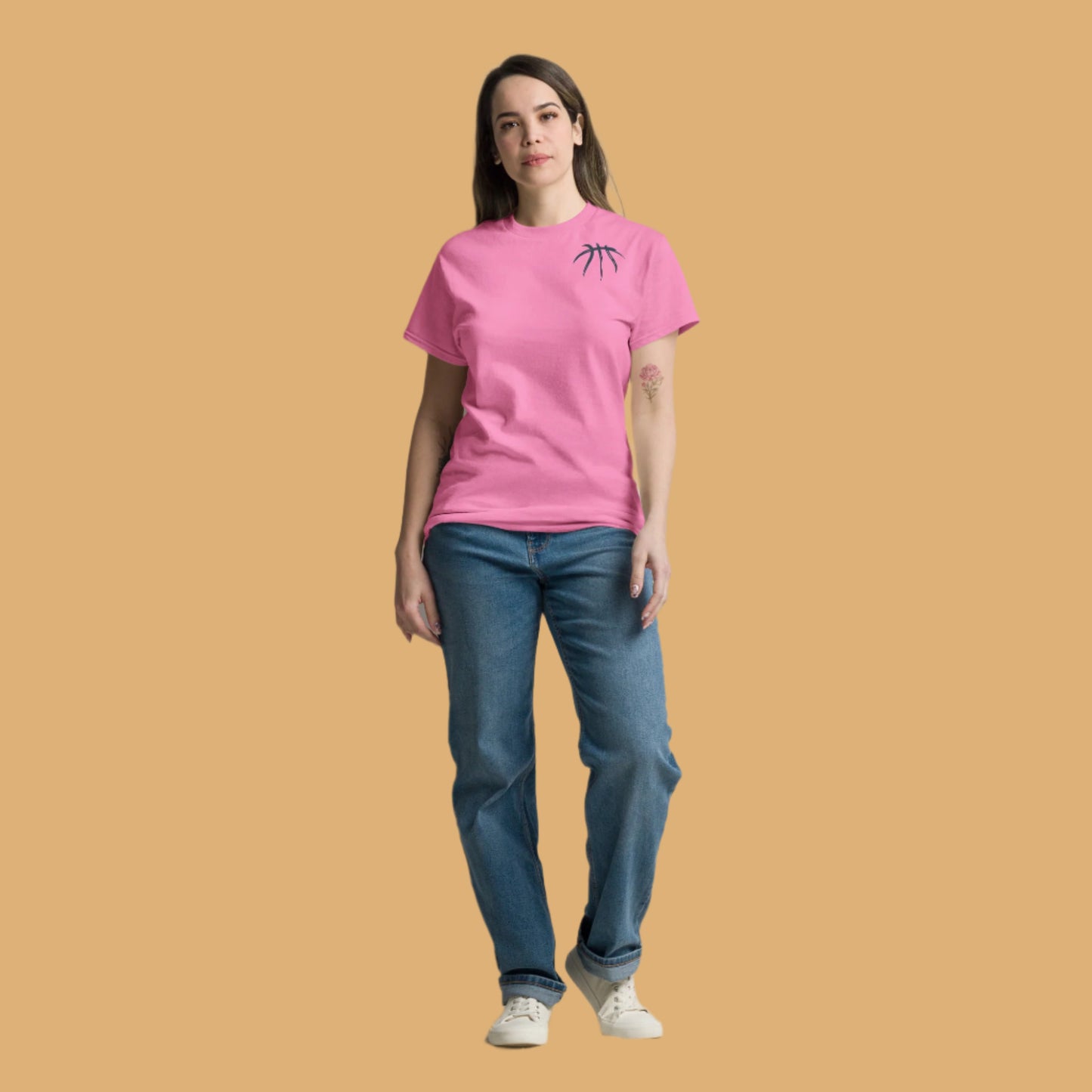 Woman wearing a pink t-shirt and blue jeans standing against a plain background