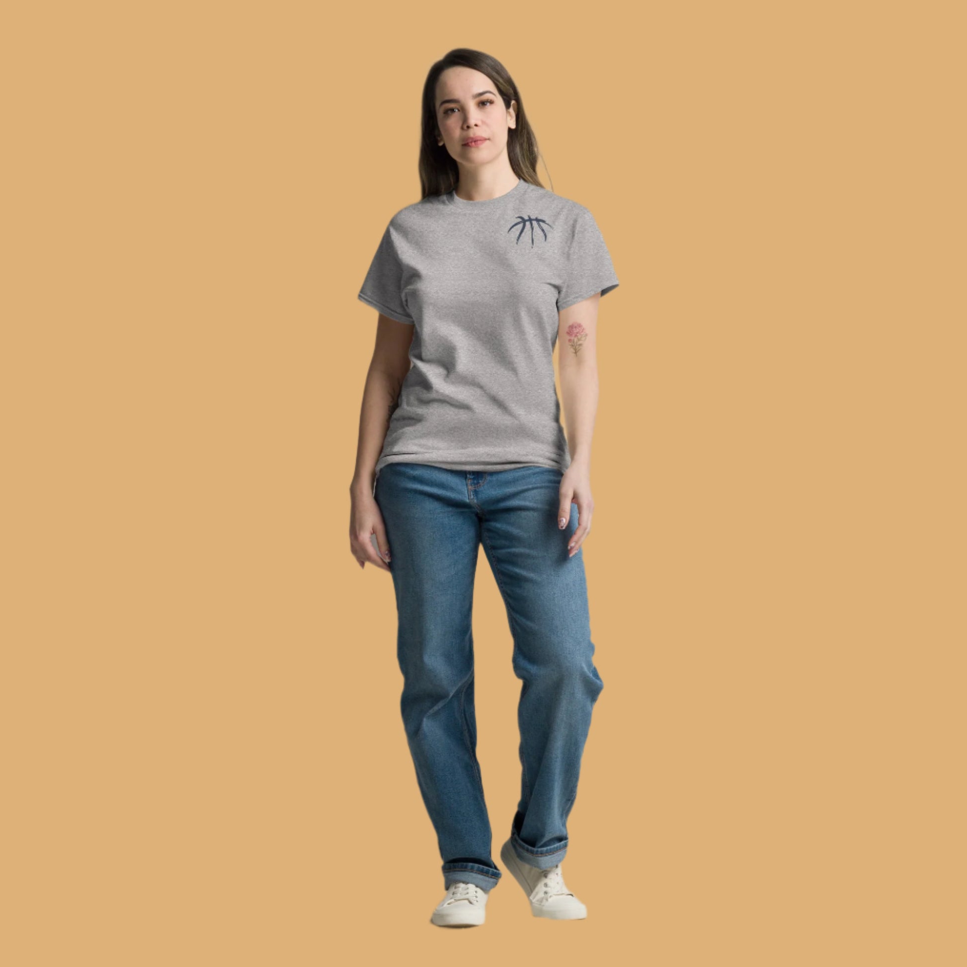 Woman wearing a gray t-shirt and blue jeans standing against a plain white curtain.
